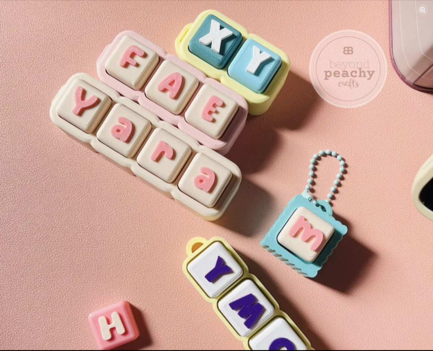 Name charm keychains laid out on a peach backdrop